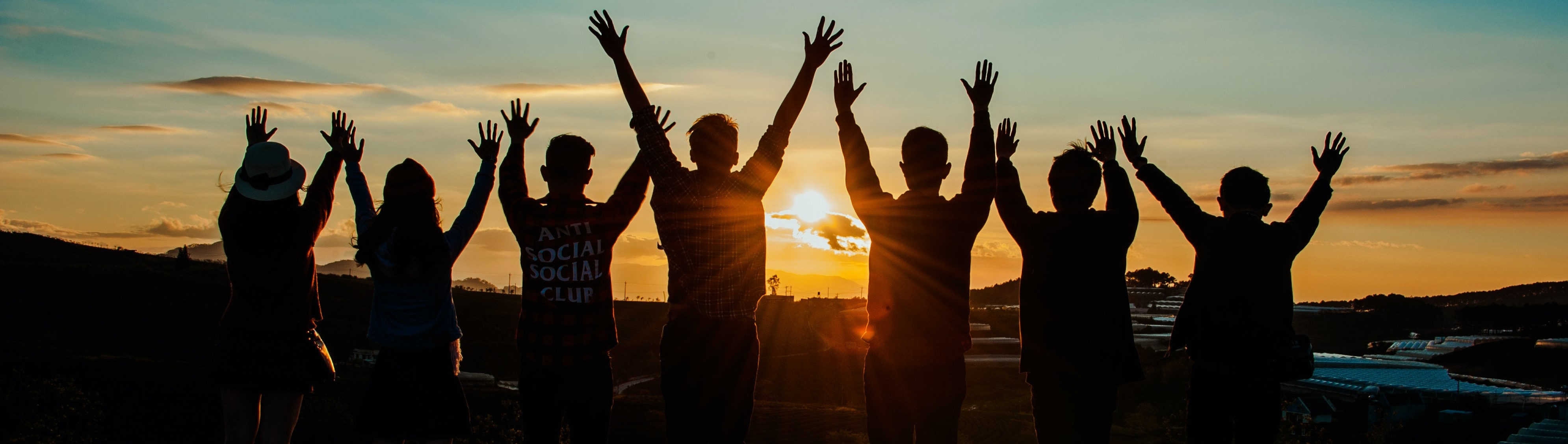 Grupopo di giovani a braccia alzate sullo sfondo di un tramonto